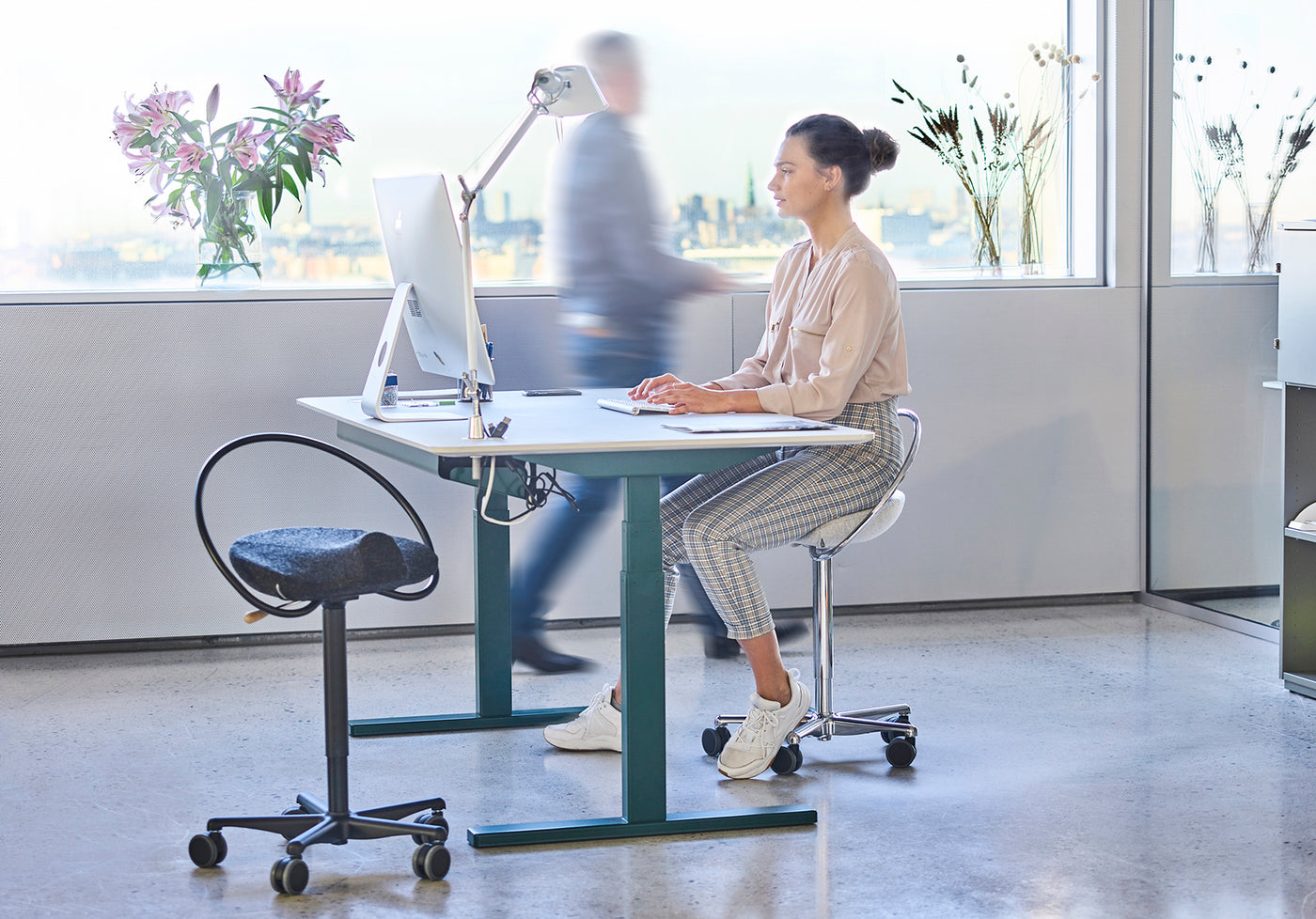 Kvinna som sitter på en InCharge Office-kontorsstol, sitsen är klädd i ljusgrå Hallingdalsull från Kvadrat. Hon sitter på ett kontor och arbetar på sin IMac.
